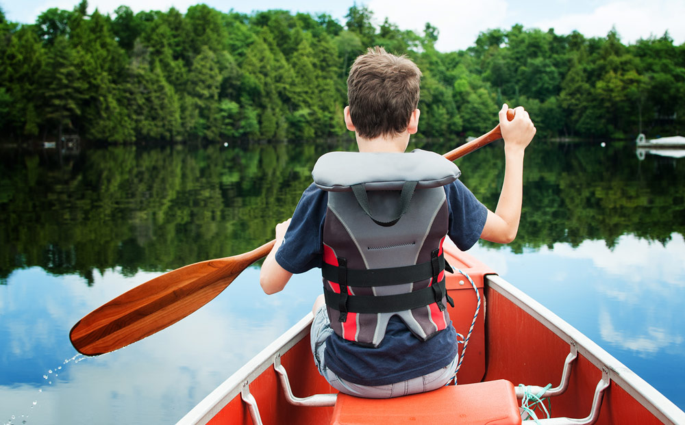 Boy in a canoe on a lake surrounded by trees.