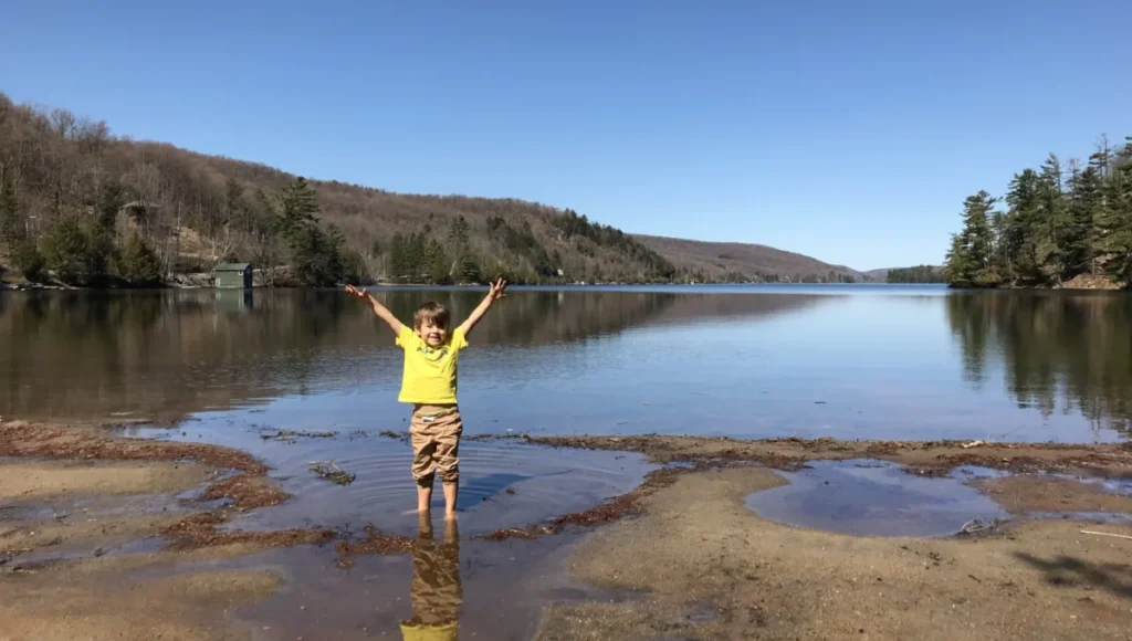 Young boy with his feet in the water on the shore of Meech Lake.