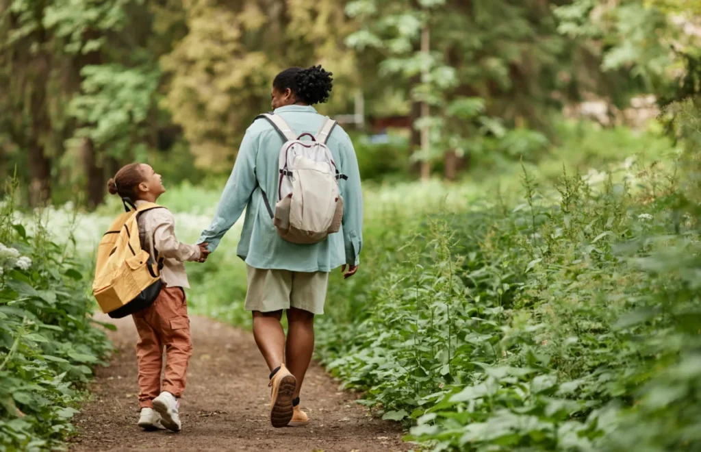 Back view of joyful mother and daughter walking on nature trail